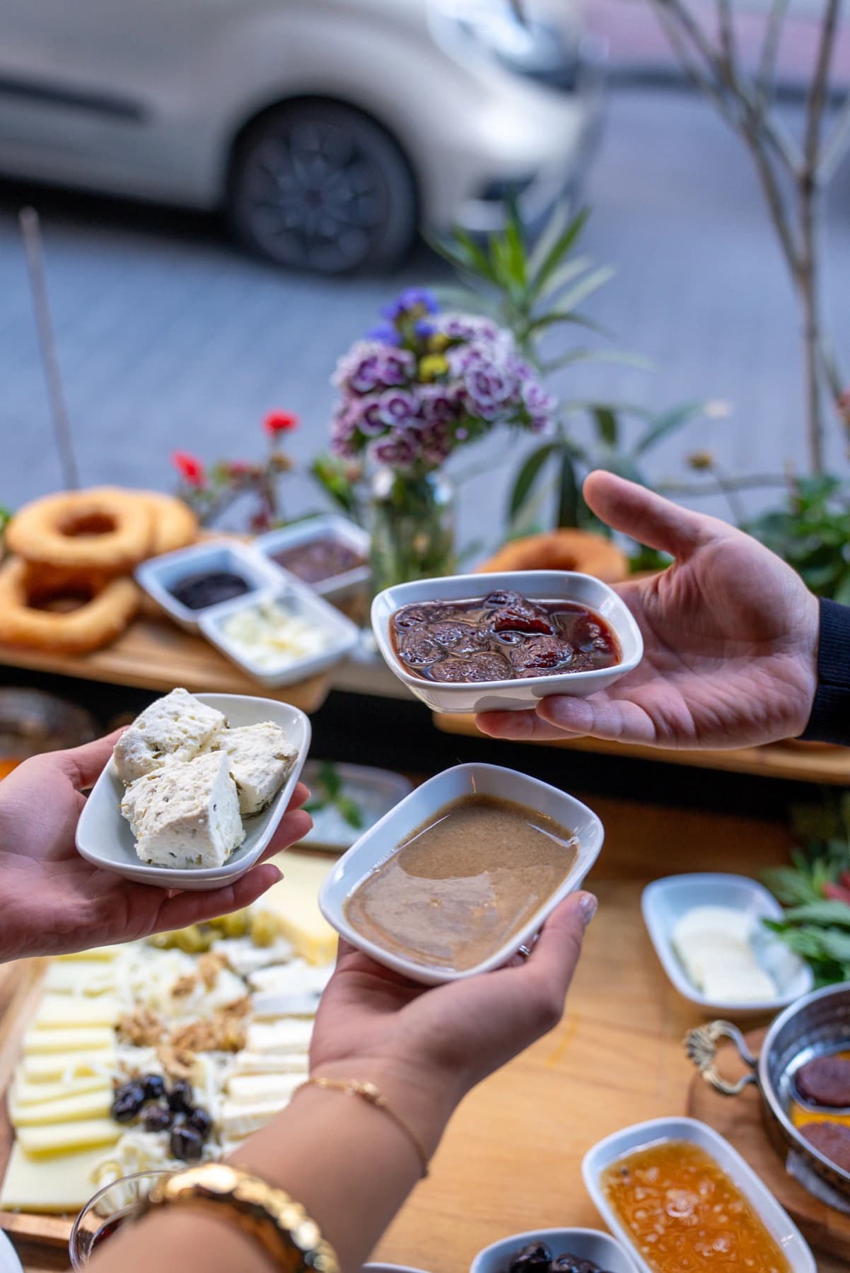 Kahvaltı sofrasında peynir, reçel ve tahin tabaklarını uzatan eller